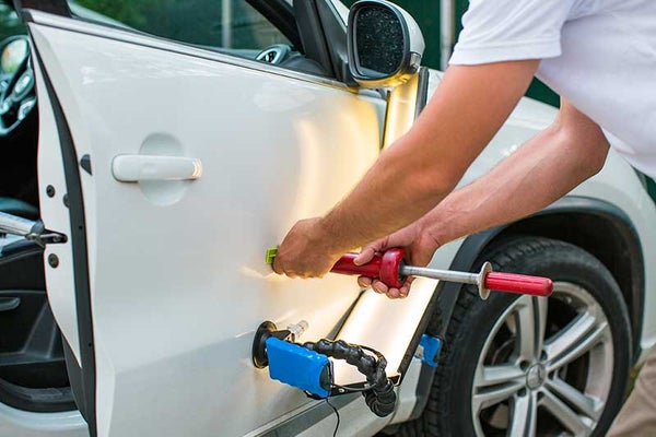 A technician pulling a dent from a car door with paintless dent repair tools