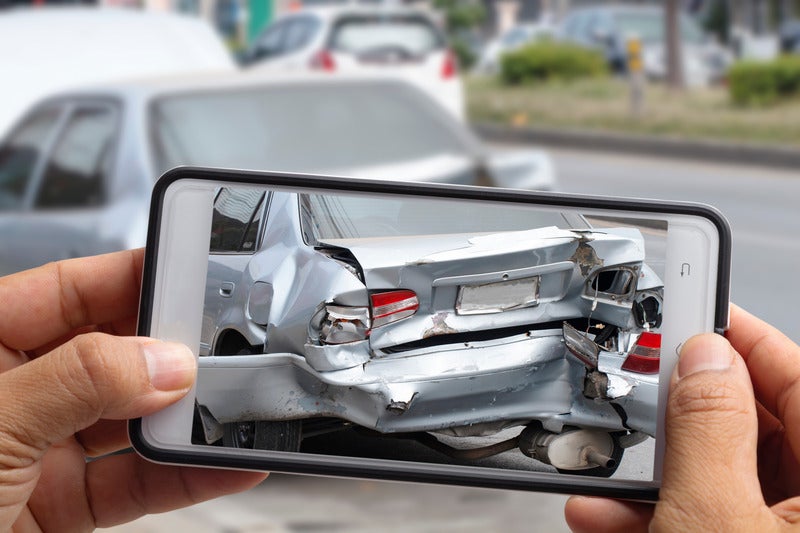 A driver photographing a damaged car on a phone for an insurance claim